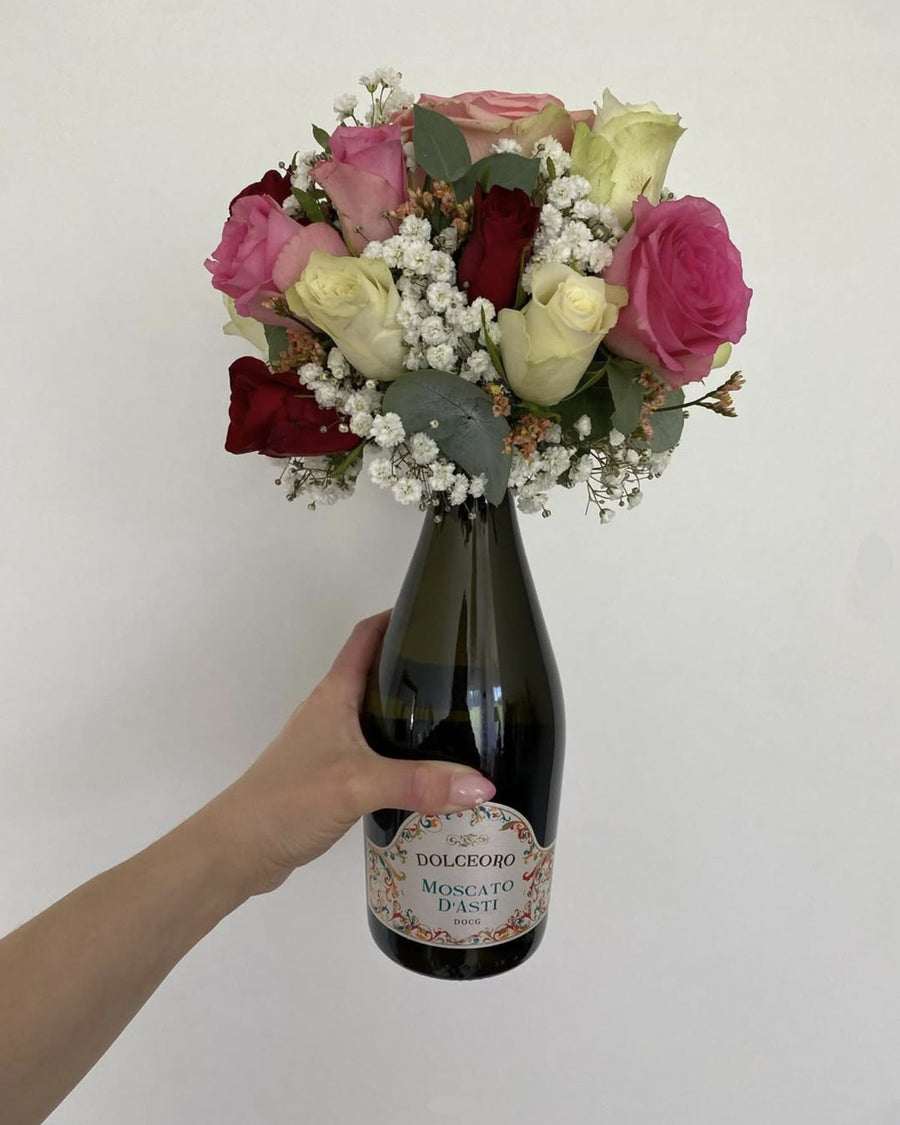 Aperol-Spritz-Flasche mit einem Strauss aus orangen und roten Rosen und weissem Schleierkraut